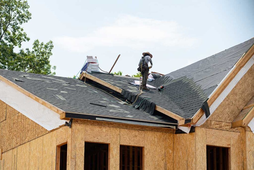 Homeowner compares roofing samples beside siding on a house exterior under natural daylight.