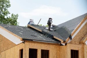 Homeowner compares roofing samples beside siding on a house exterior under natural daylight.